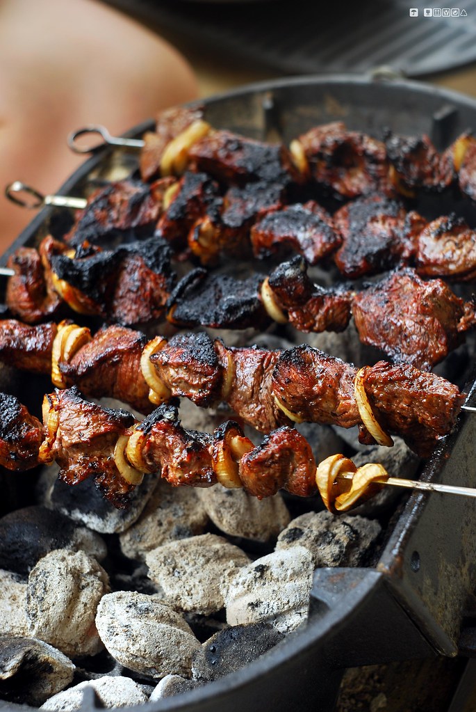 Meat kebabs grilling over charcoal with flames and ash visible